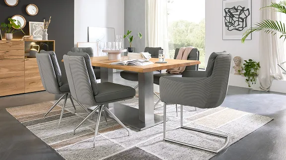 Ein Esszimmer mit gepolsterten grauen Stühlen und einem Tisch mit Holzplatte der Serie 5116